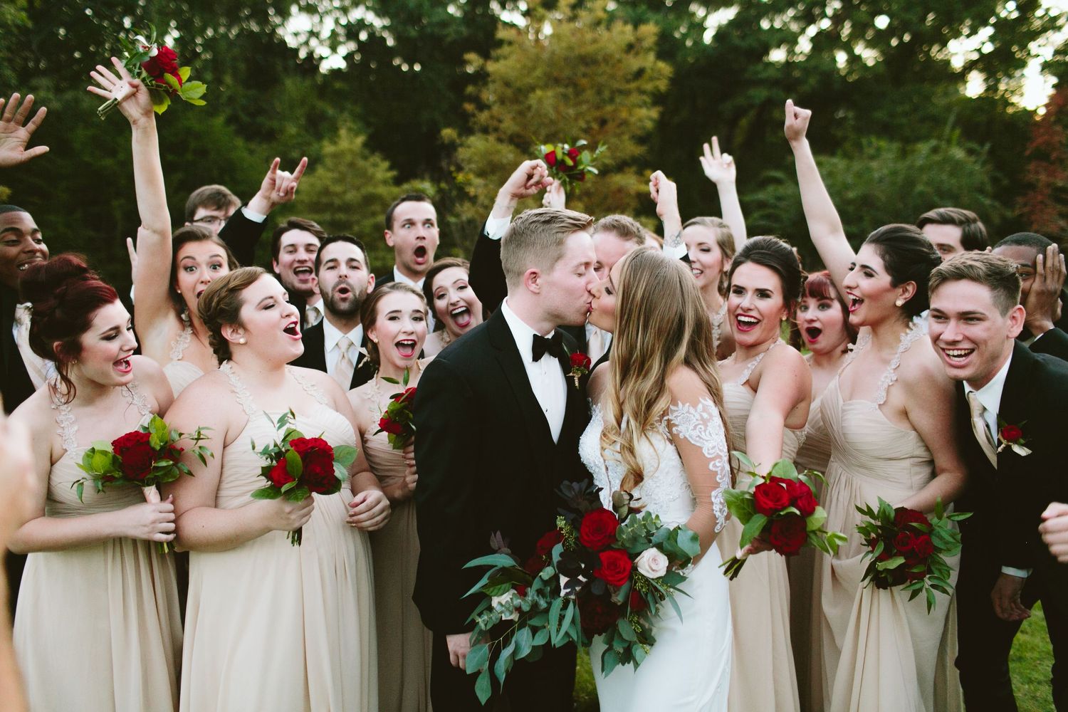 Newlyweds celebrate with their wedding party as bridesmaids in beige dresses cheer with raised arms.