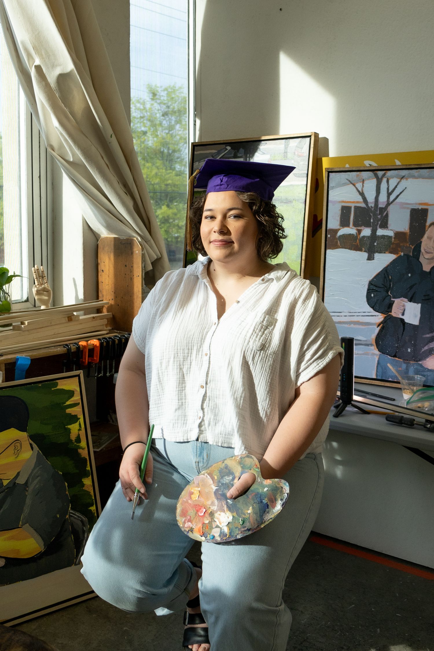 An art student graduate sits in front of her work in her studio creating a portrait based on location.