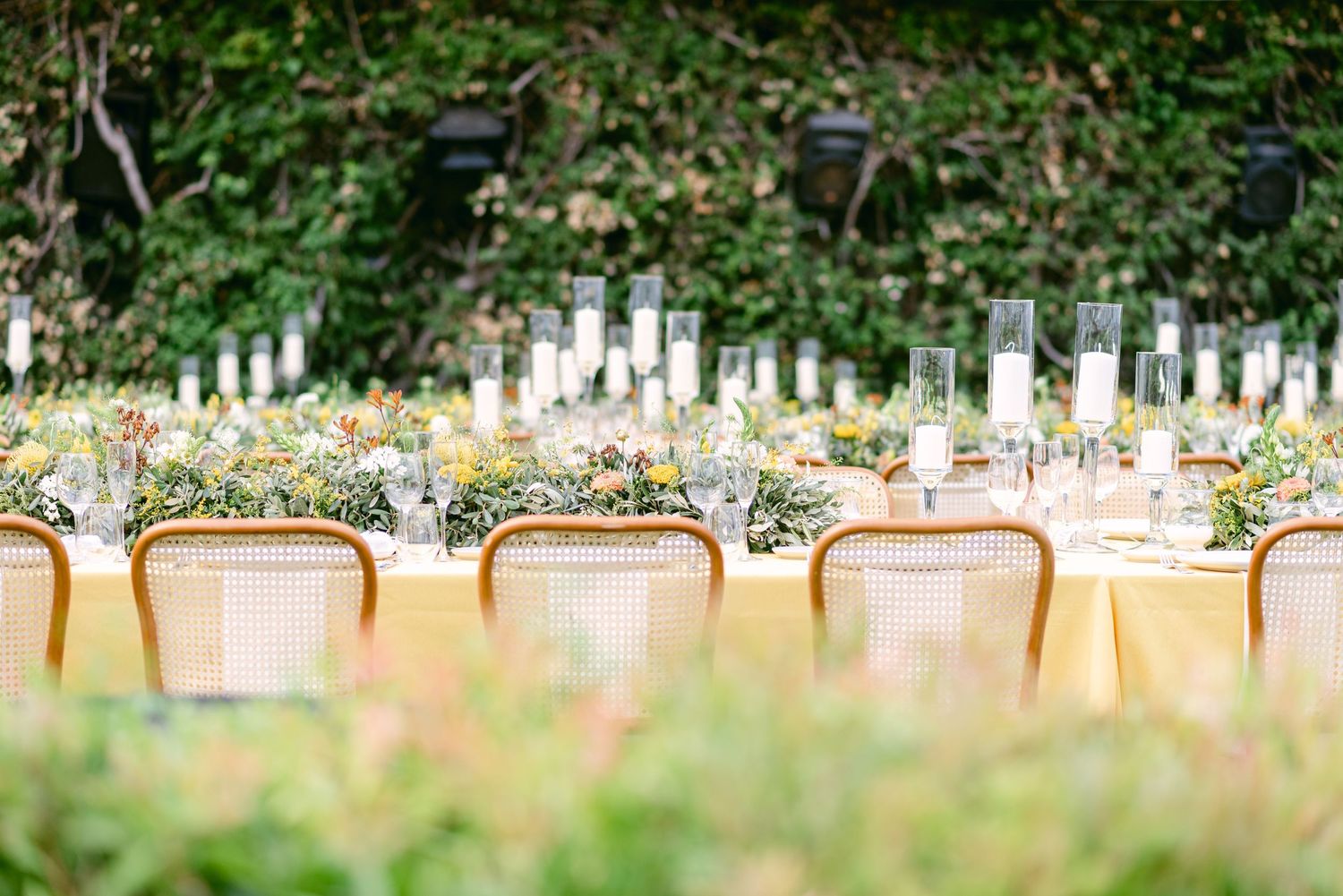 Elegant outdoor dining setup with cane chairs and floral centerpieces along a table.