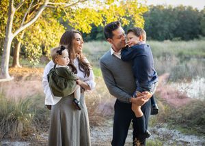 A romantic couple embraces in a sunlit meadow during golden hour with autumn foliage in the background.