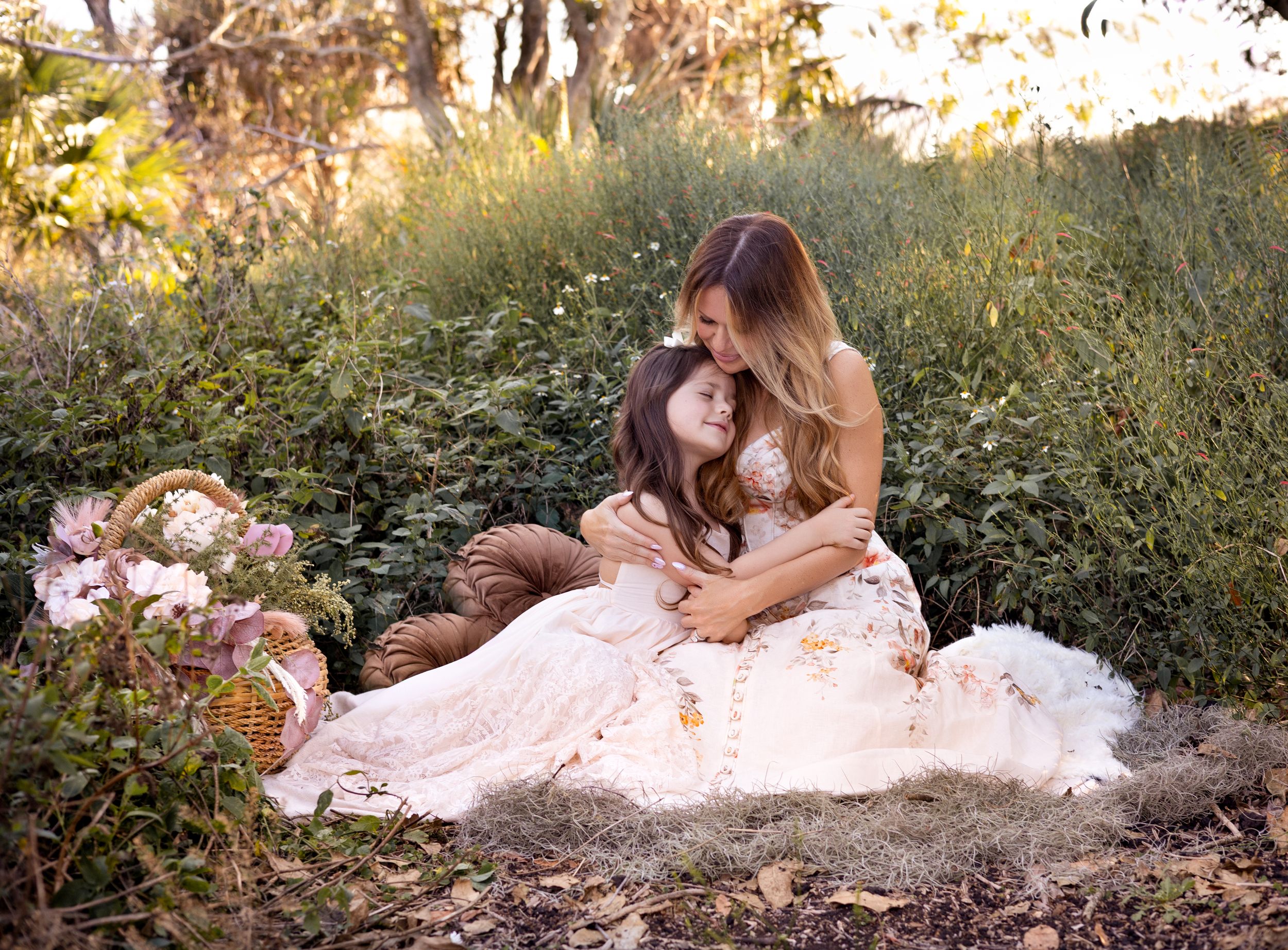 Two figures in pink dresses sit together in a dreamy garden setting with lush greenery and flowers at sunset.