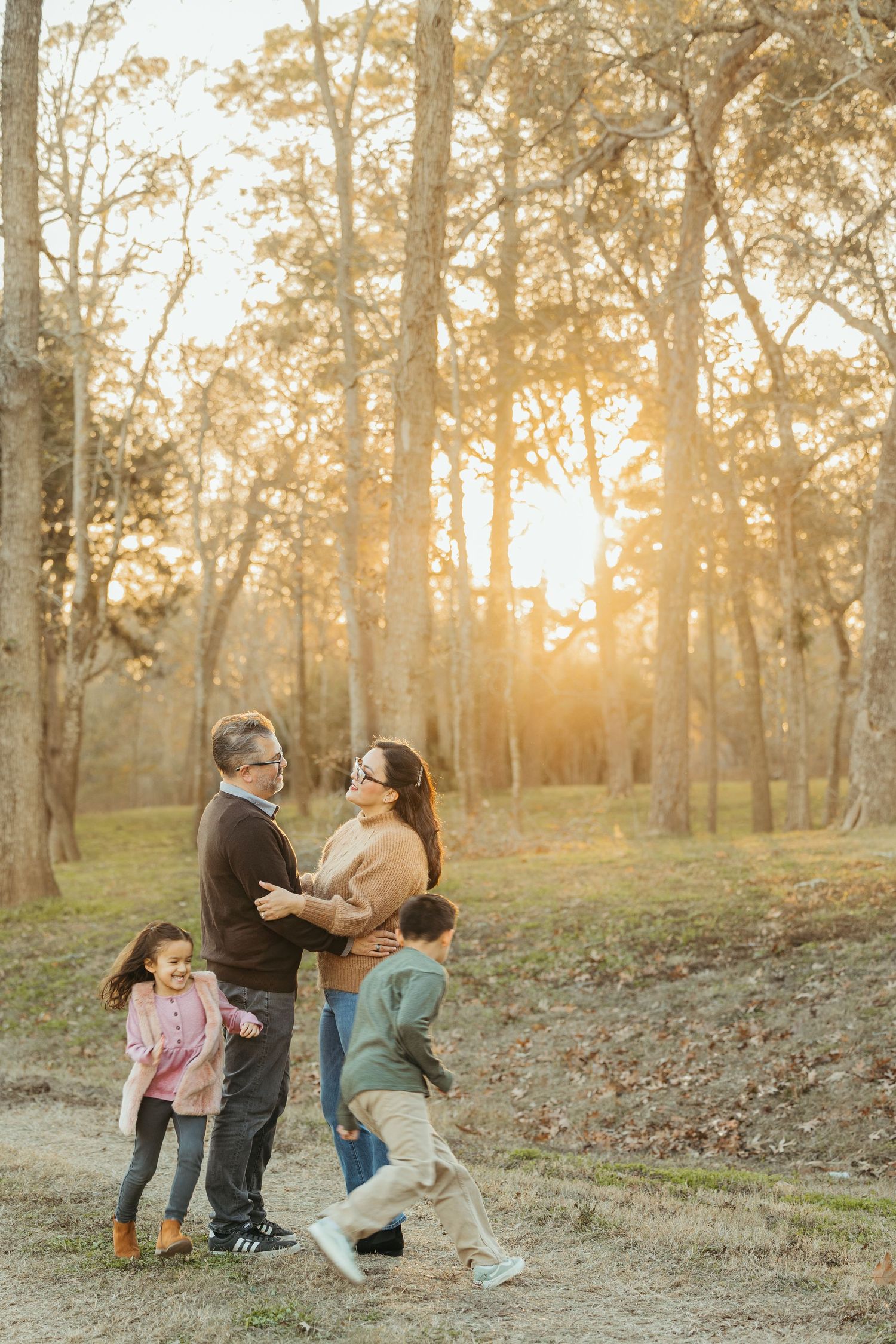 Grandparents smiling with two grandchildren during a golden hour family portrait in a wooded park.