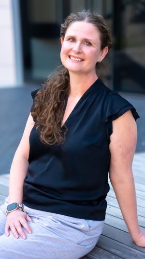 Professional headshot of someone in a navy blouse sitting outdoors.