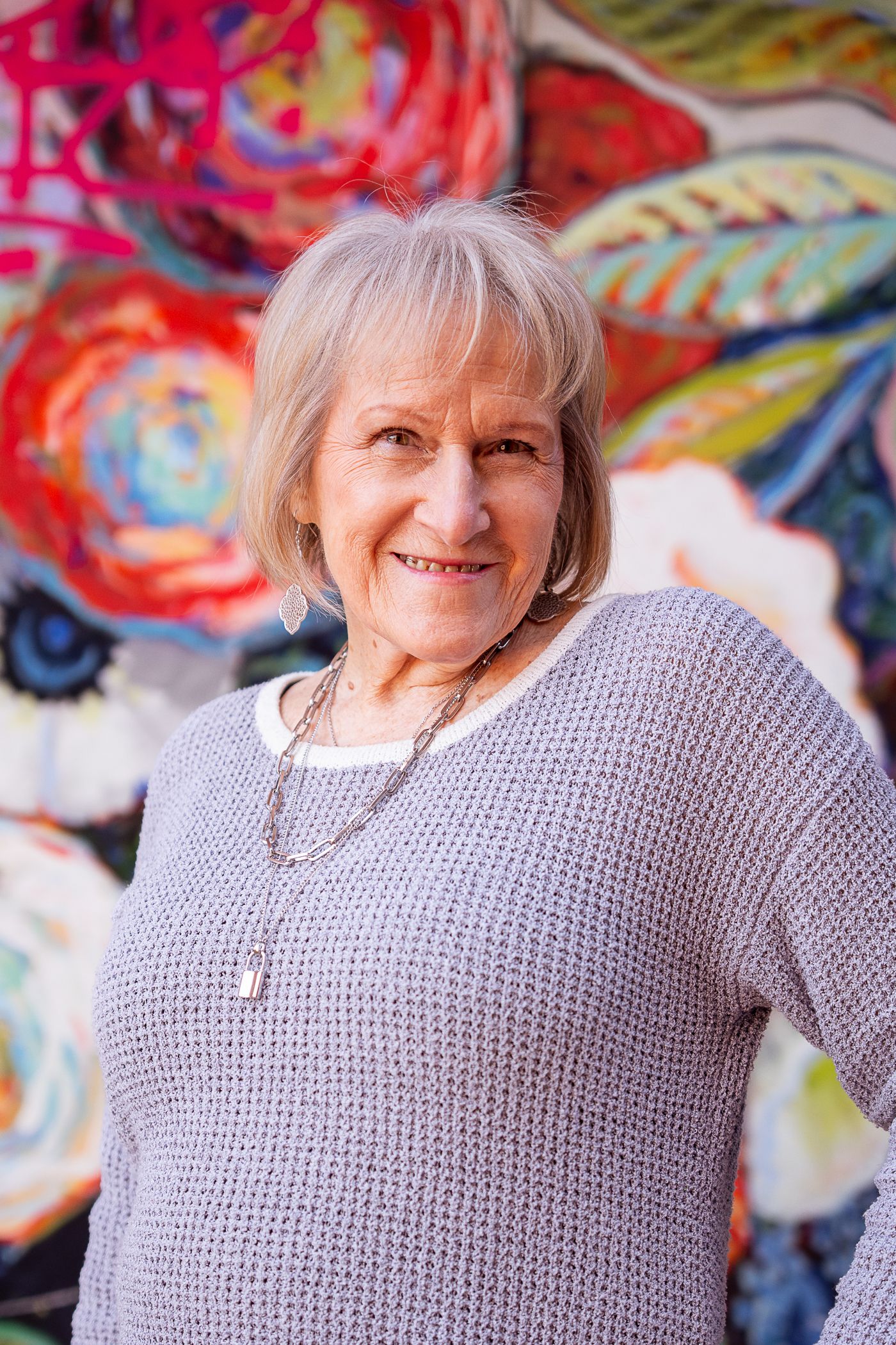 A person wearing a gray knit sweater poses against a vibrant abstract art background with colorful swirls and patterns.