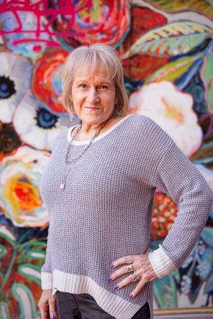 A person in a gray knit sweater poses against a colorful floral mural background.