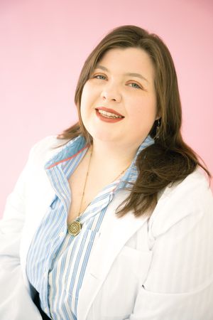 Professional wearing blue striped shirt and white coat poses against pink background in expressive portrait series.