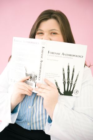 A person holding a Forensic Anthropology textbook with an X-ray hand image on the cover against a pink background.