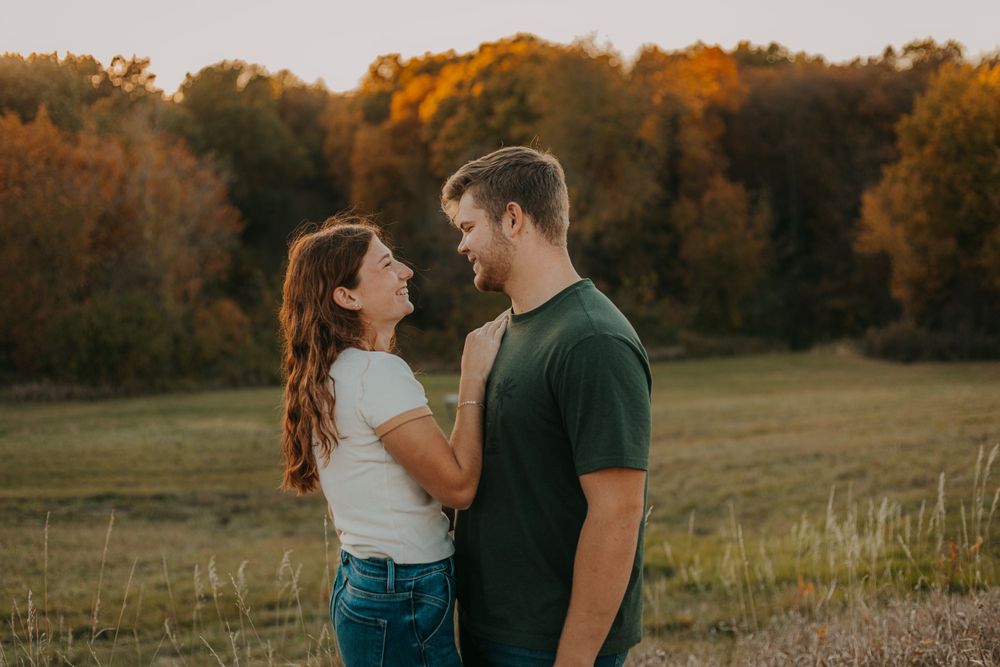 A couple shares an intimate moment while standing in a field at sunset.