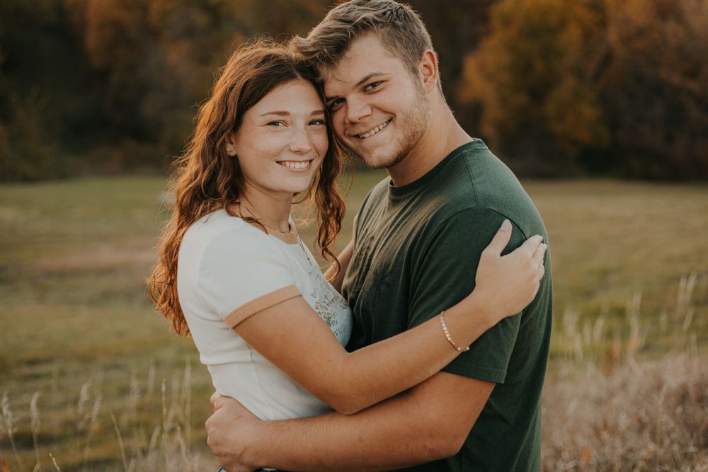 A couple embraces warmly while sharing an intimate moment in a sunny autumn field.