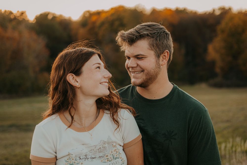 A couple shares joyful expressions while posing together in warm evening sunlight.