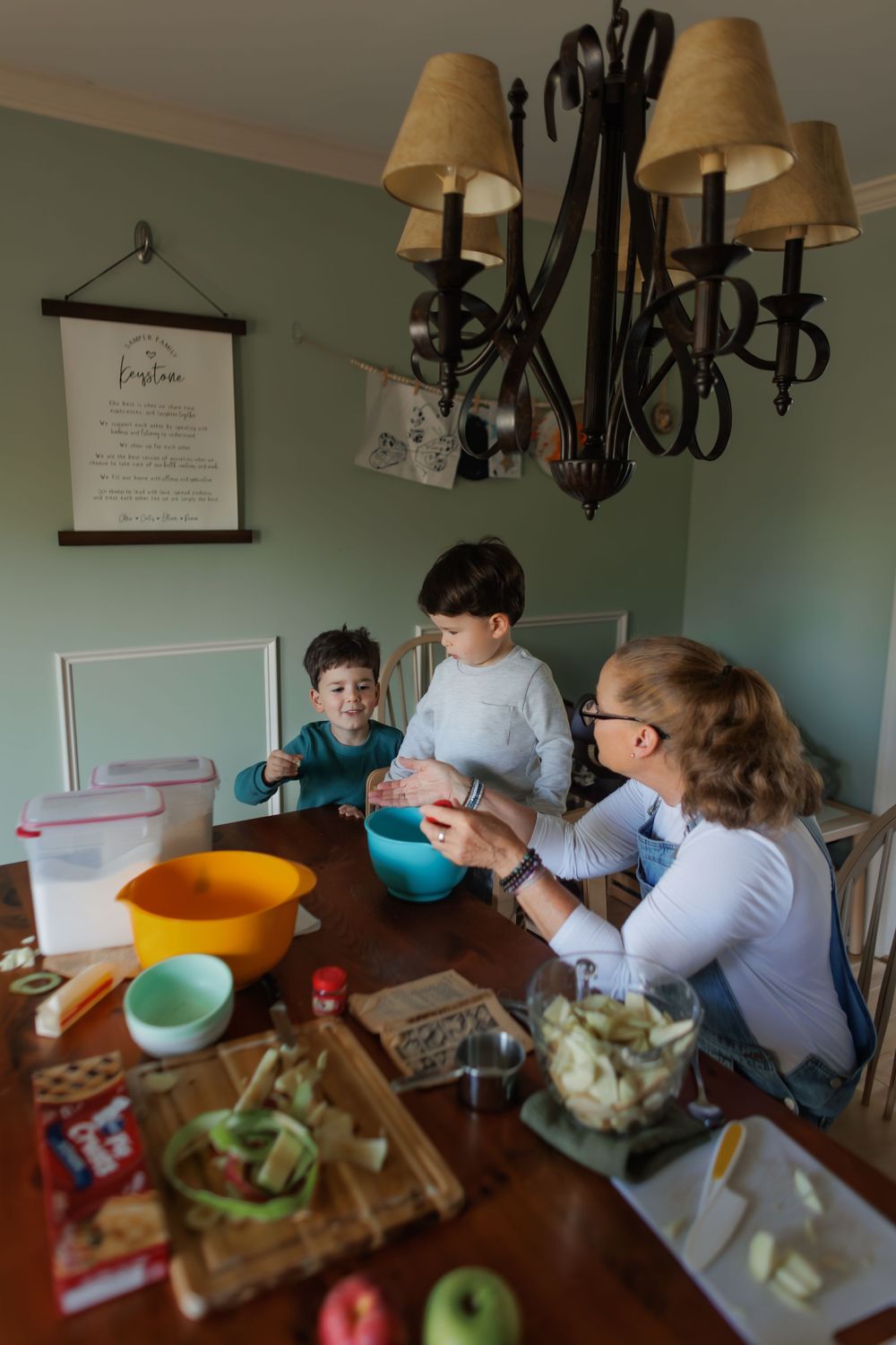 Children gather around a wooden table with colorful mixing bowls and ingredients preparing food in a home kitchen.