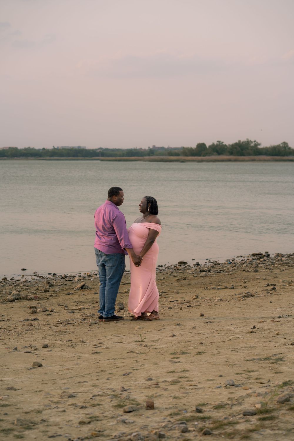 Couple in coordinating pink outfits stands together on a beach shoreline during sunset.