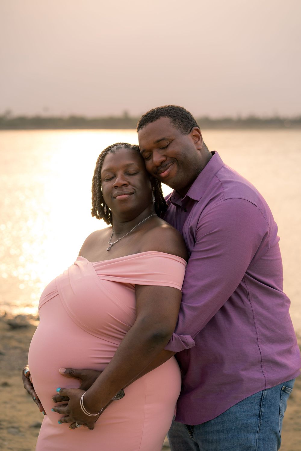 Romantic sunset maternity photo of couple sharing tender moment on beach.