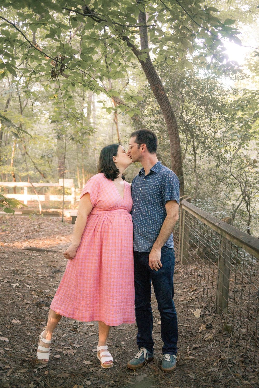 A couple in pink dress and blue shirt sharing romantic moments on a wooded path.