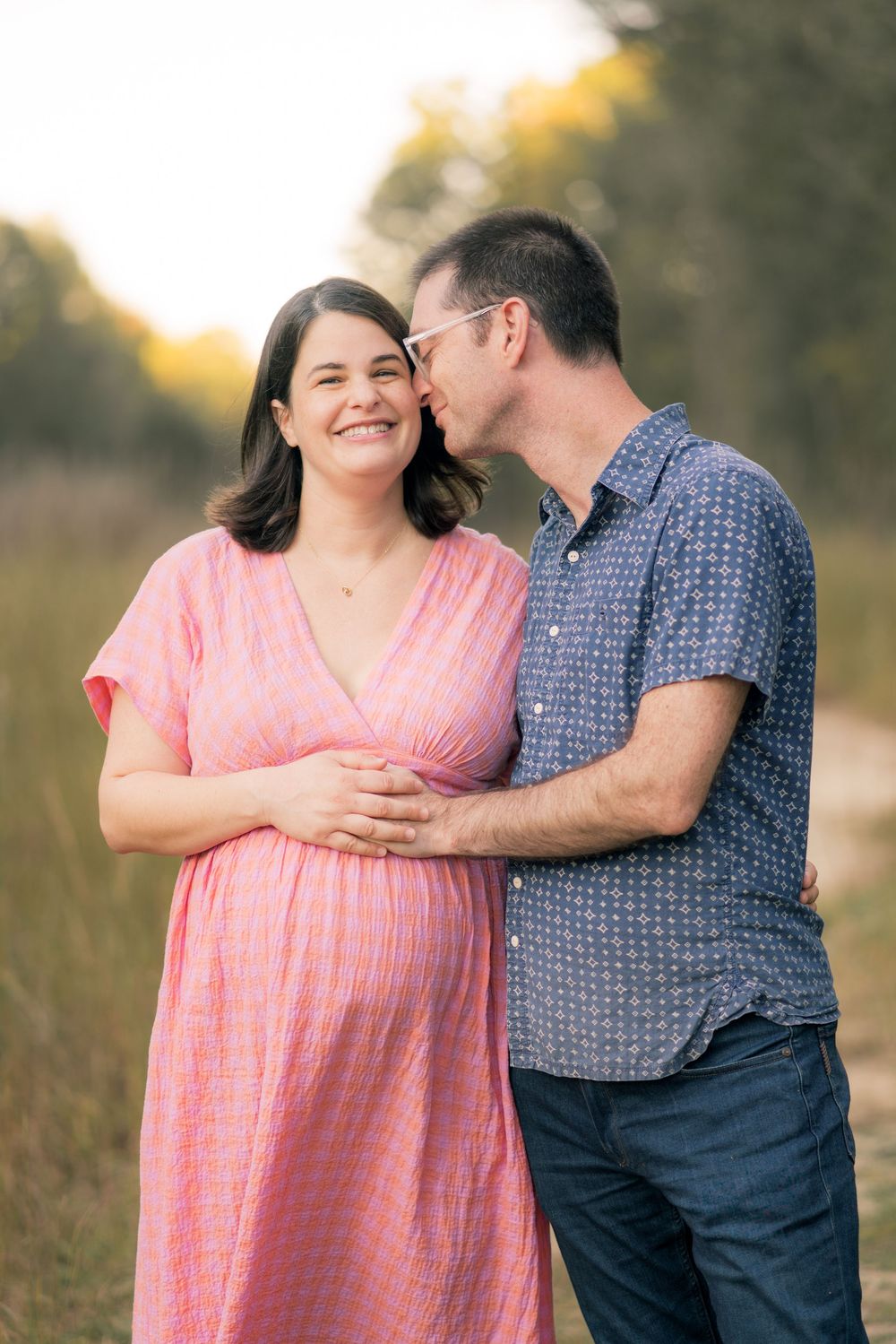 Expecting couple embraces tenderly in a field during golden hour maternity photoshoot.