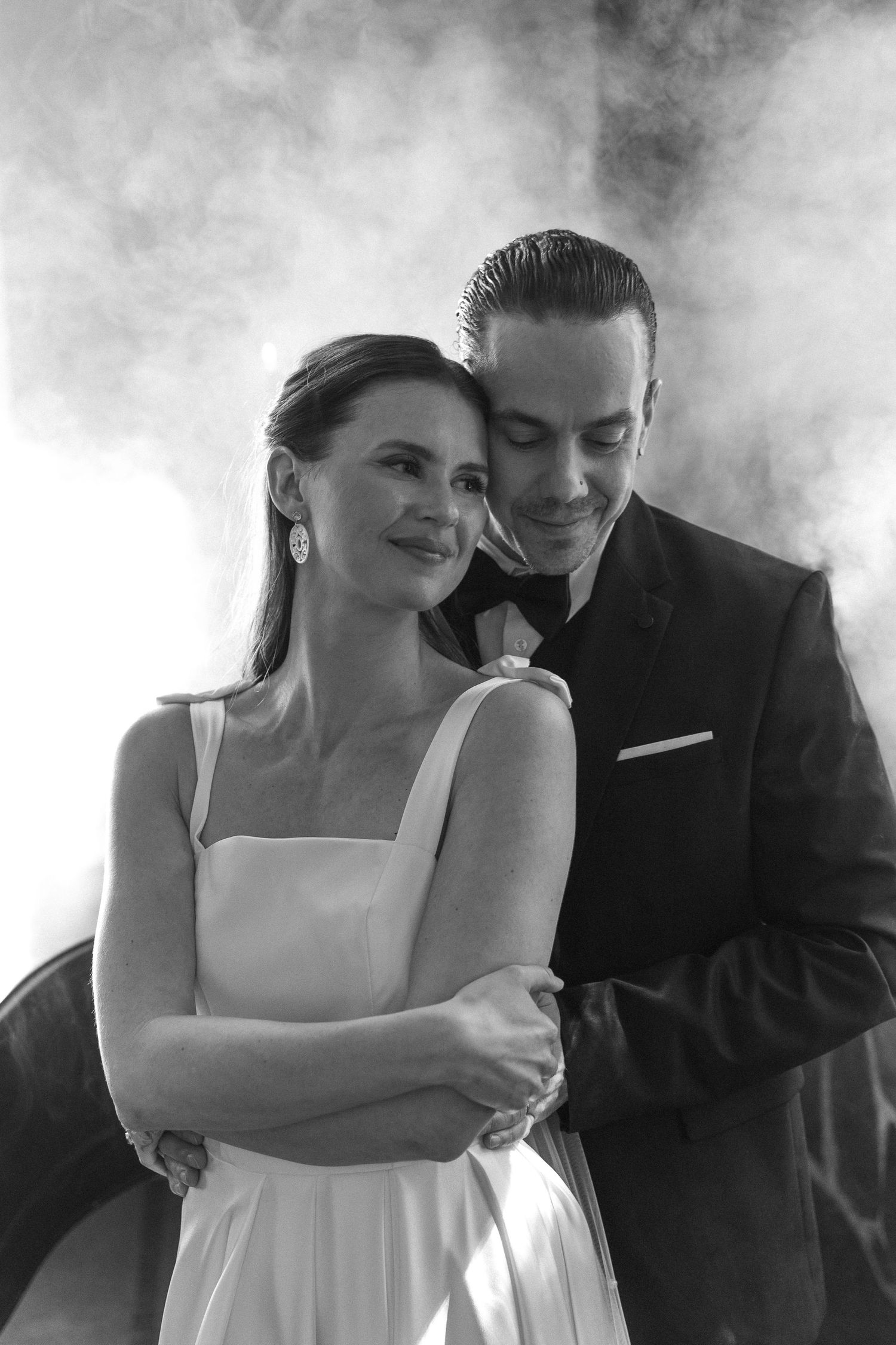Artistic black and white portrait of a bride and groom embracing in romantic smoky atmosphere.