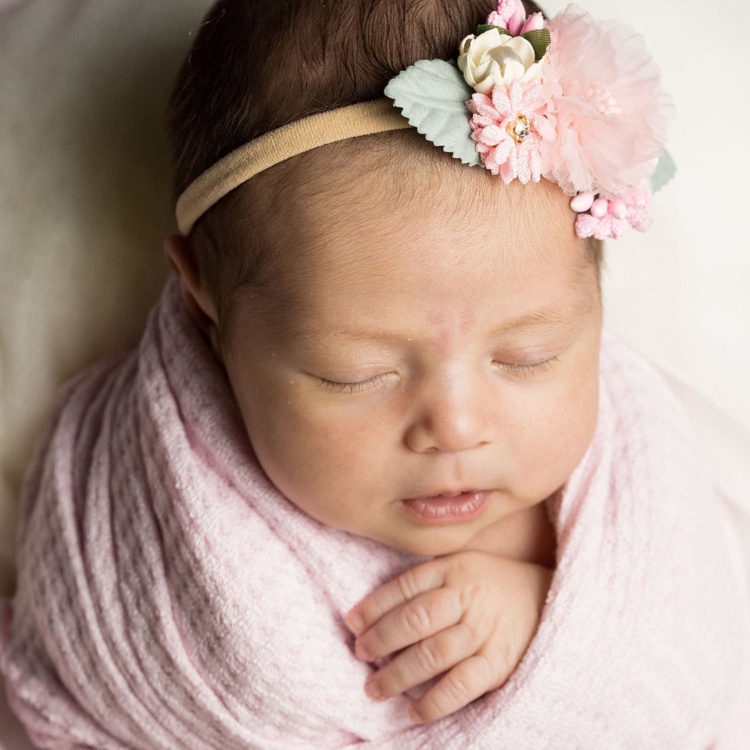 Sleeping newborn wearing pink floral headband wrapped in soft pink blanket.