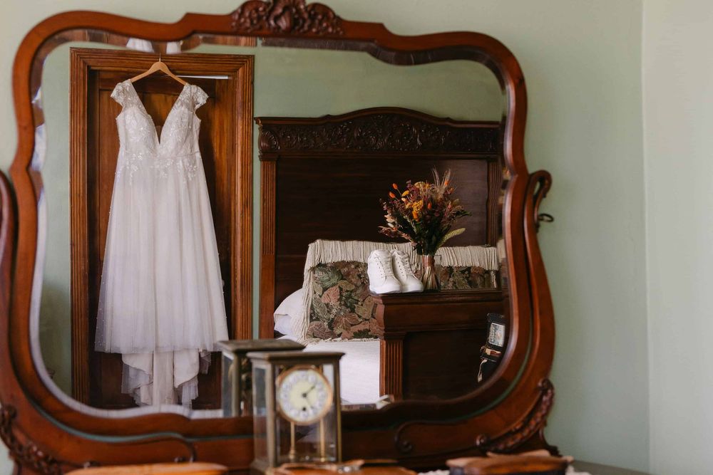 Ornate wooden mirror frames hang on mint green wall above white clothing displays in vintage-style room.