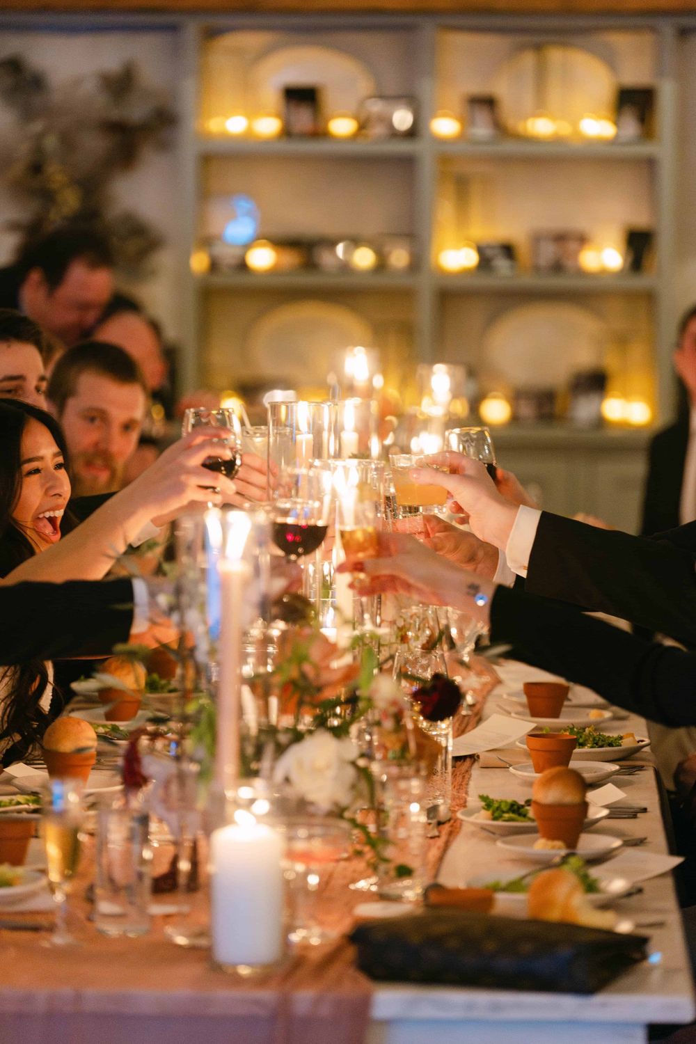 Wedding reception dinner table with candlelight and guests toasting wine glasses in an intimate setting.