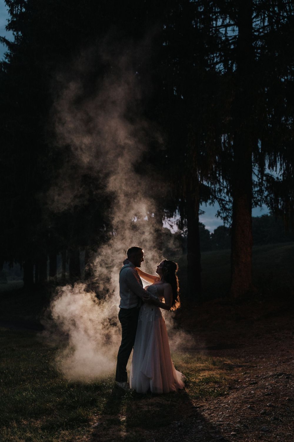 A romantic silhouetted couple dances in a misty forest setting at dusk with ethereal smoke surrounding them.