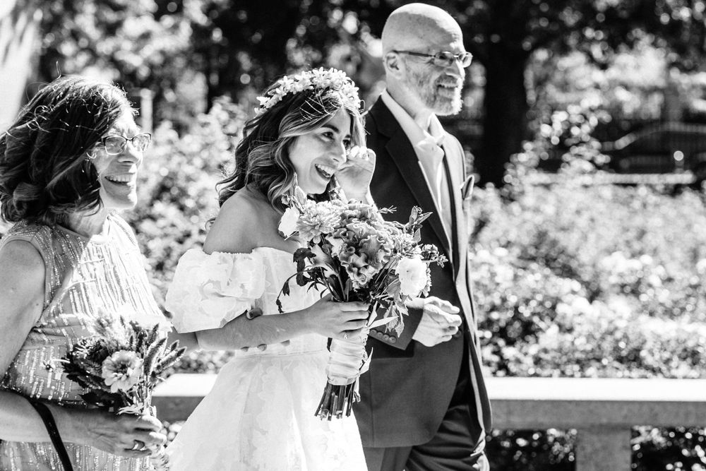 A joyful moment captured in black and white as people walk together at a wedding ceremony while holding floral bouquets.
