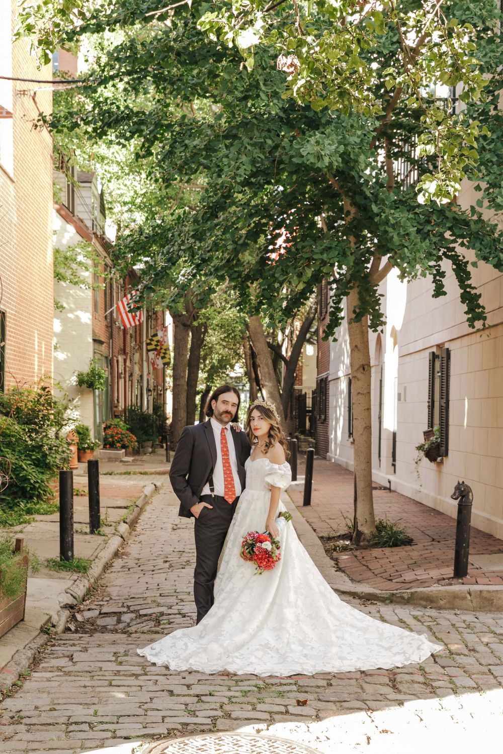 A wedding couple stands on a charming cobblestone street lined with trees and historic buildings in Philadelphia.