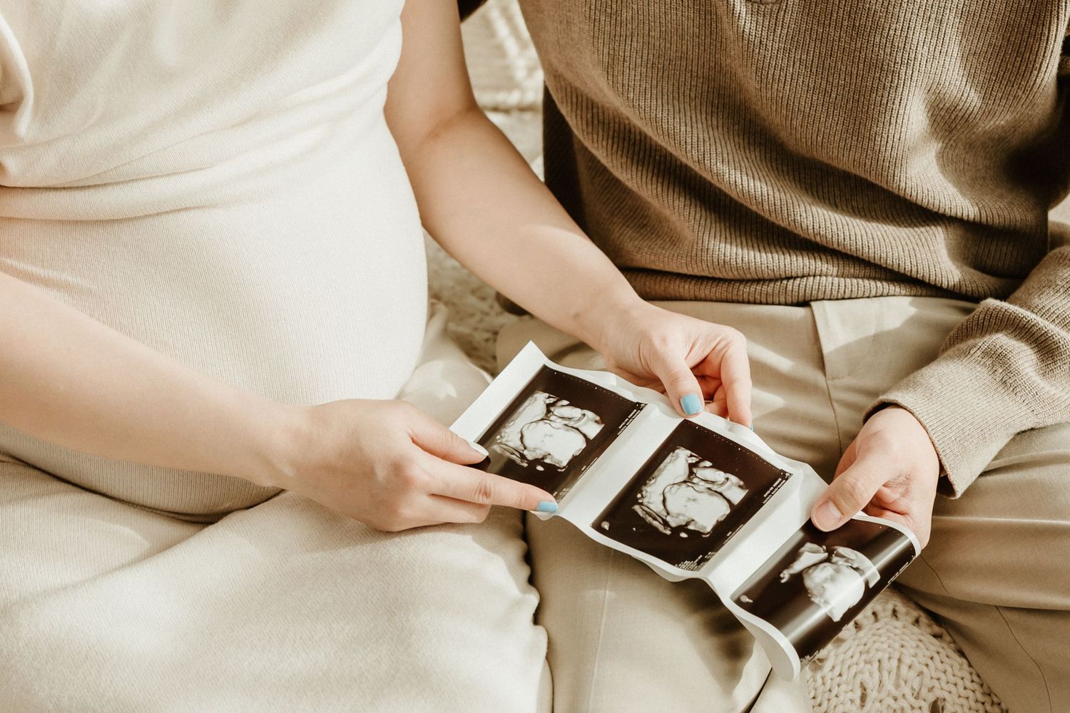Couple viewing ultrasound photos while sitting together on couch during pregnancy photoshoot.