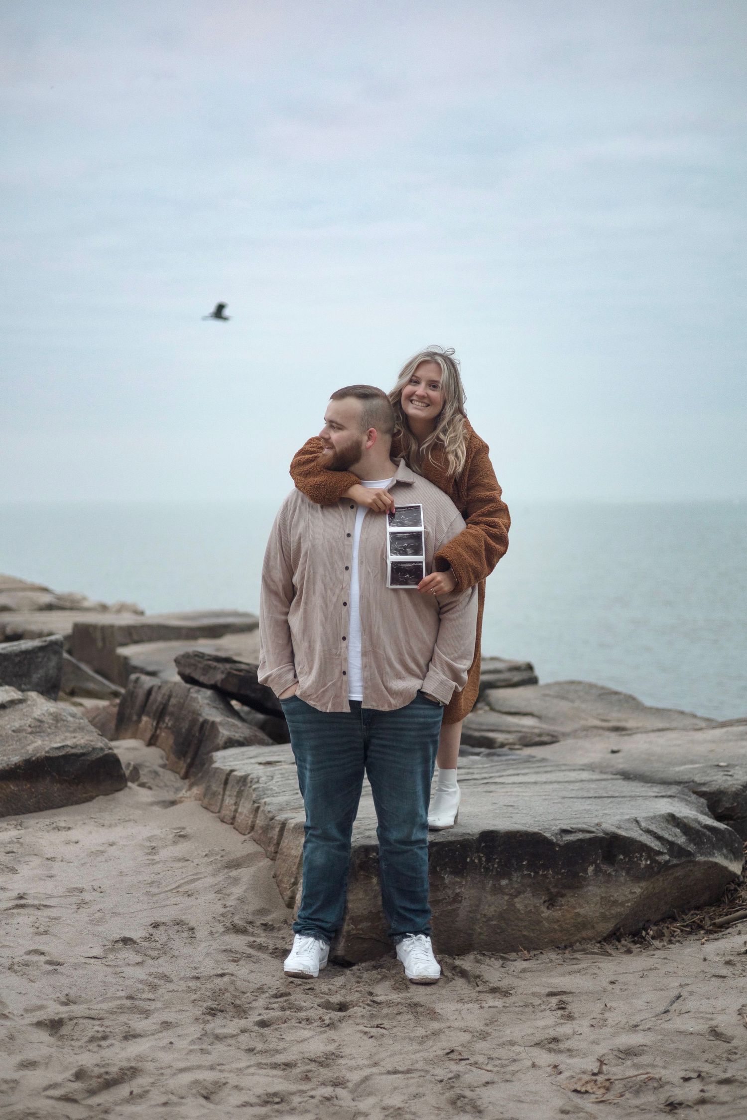 Romantic coastal photoshoot on rocky beach with overcast sky.