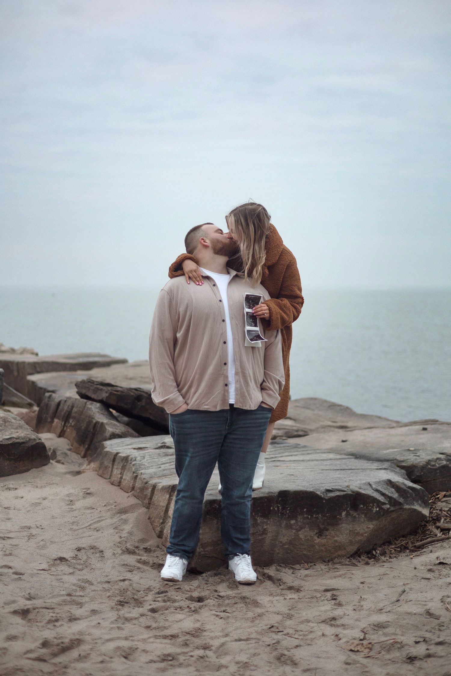 Intimate couple's portrait on rocky beach shore with ocean backdrop.