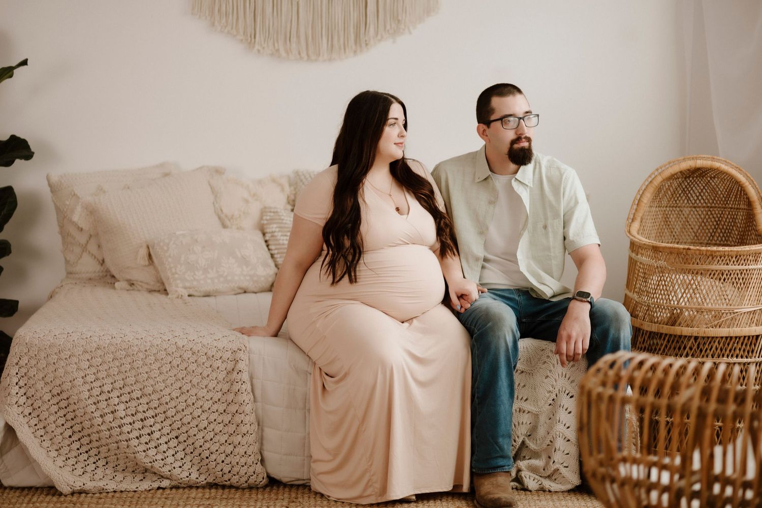 Maternity photo session with couple sitting on couch with bohemian peacock chair decor.