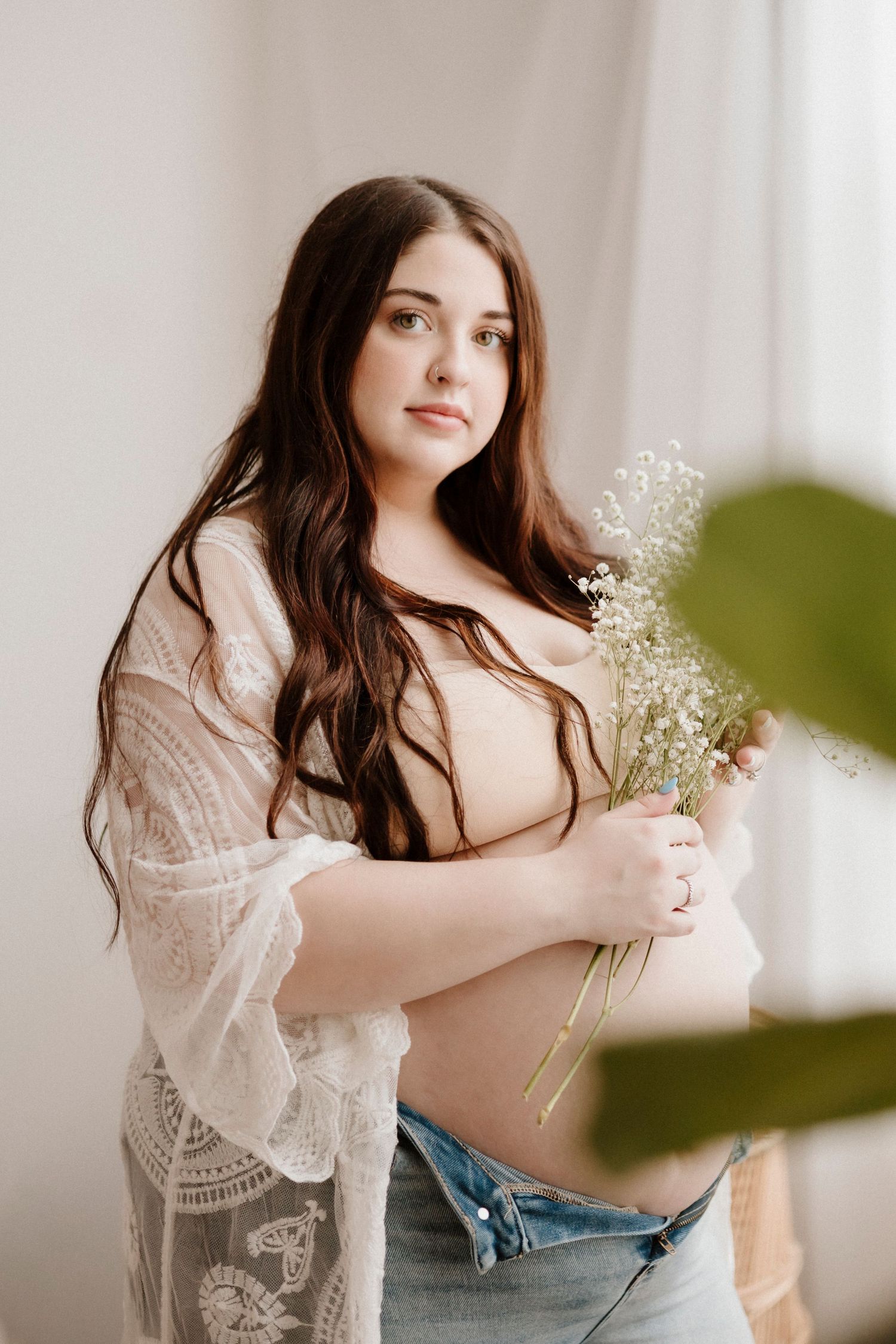 Maternity portrait with delicate lace details and baby's breath flowers against light backdrop.