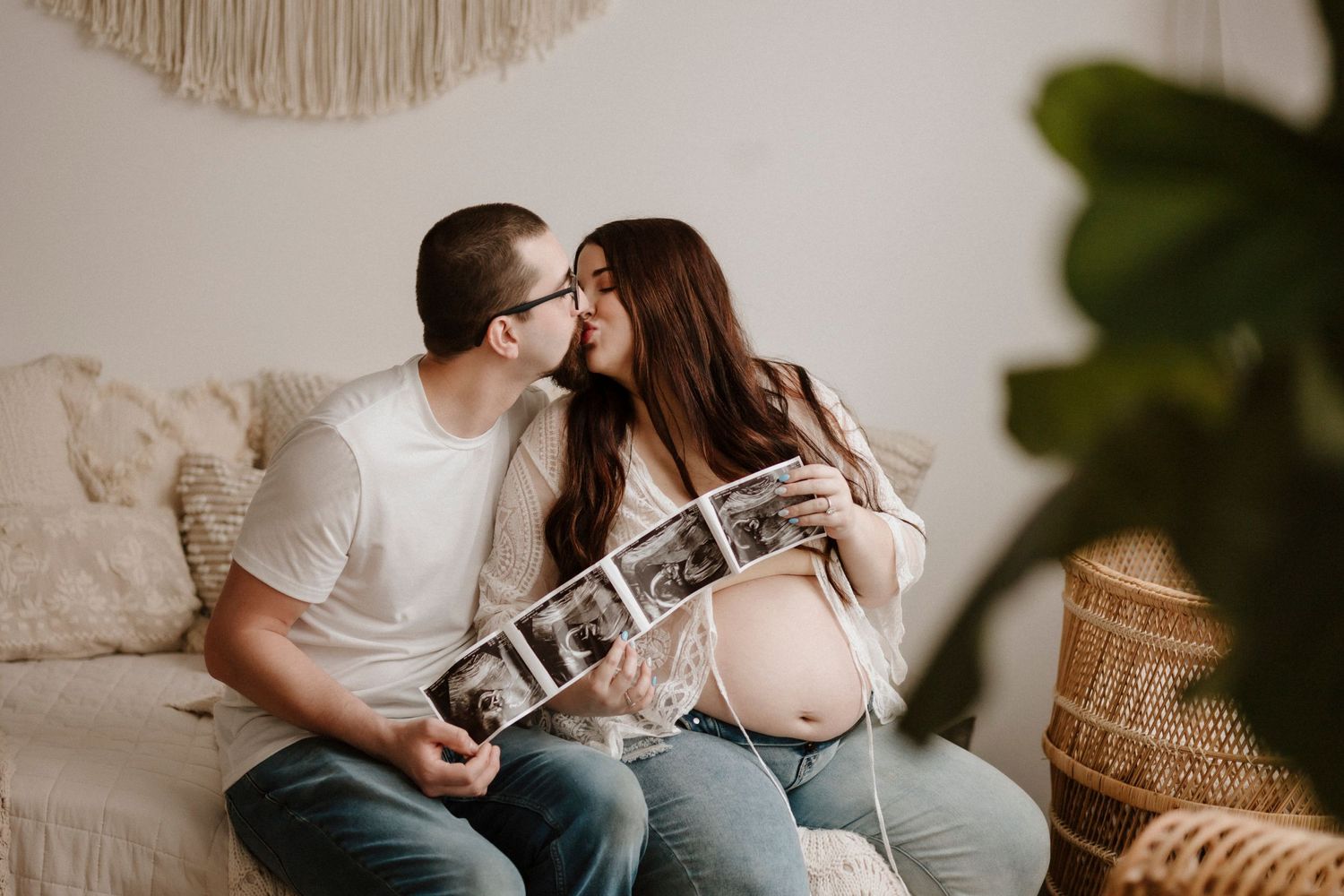 Intimate maternity shoot featuring couple on couch sharing ultrasound photos.