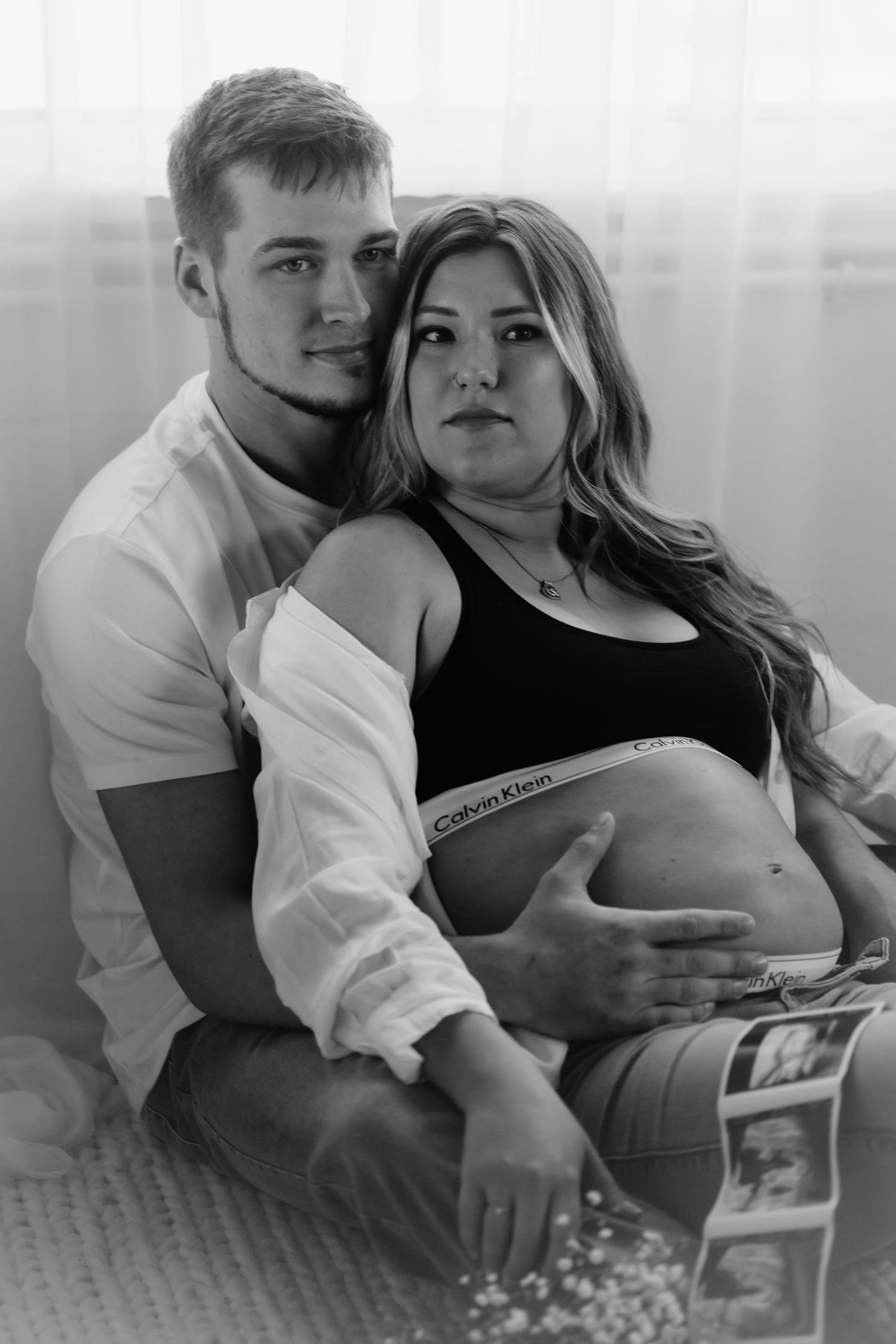 Black and white maternity portrait of couple sitting together with ultrasound photos.