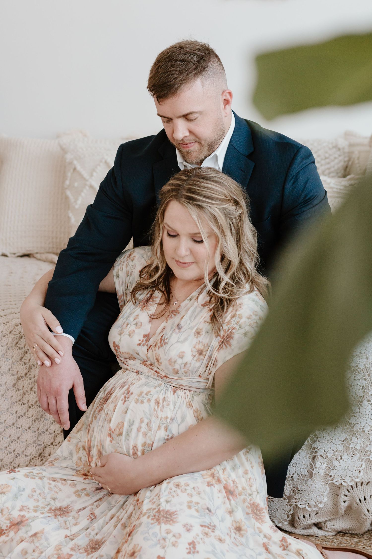 Intimate indoor maternity photo with couple on couch in soft lighting.
