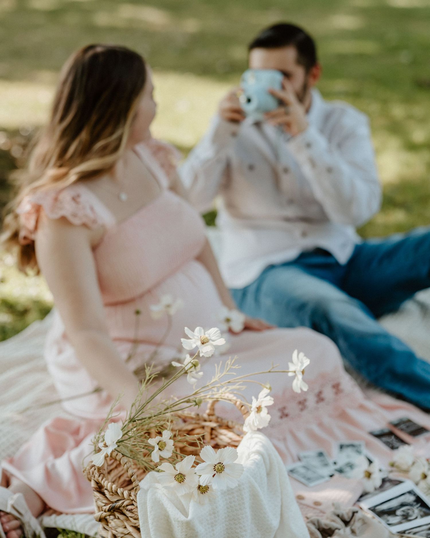 Couple enjoying a romantic picnic on a blanket with white flowers and a blue instant camera.