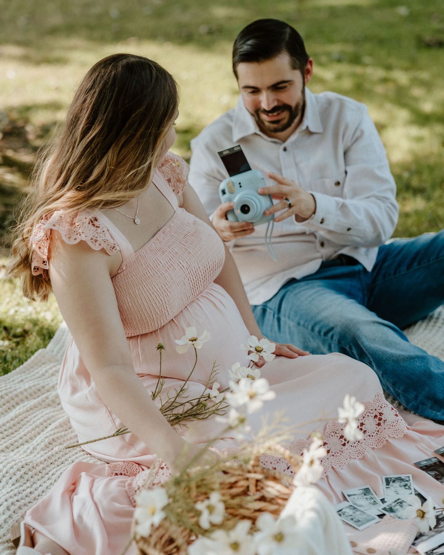 Couple sharing a moment while taking pictures with a blue instant camera on a picnic blanket.