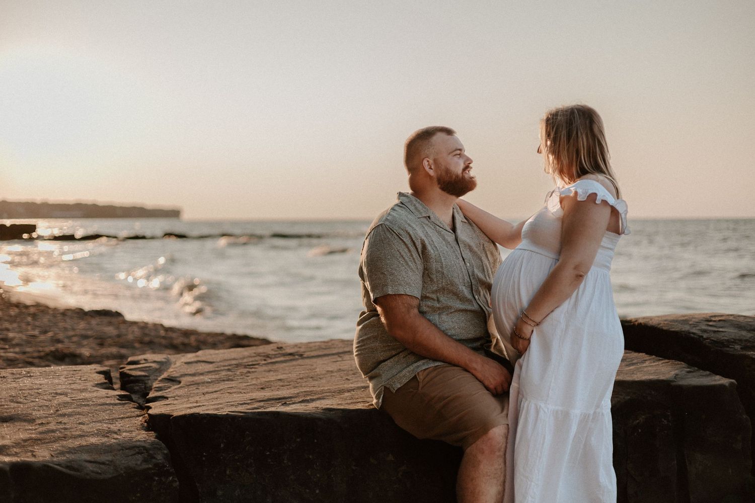 Couple embracing on rocky beach during golden hour with ocean waves in background.