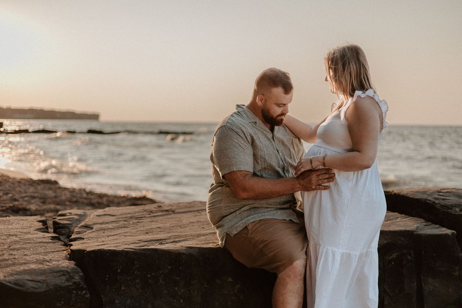 Couple sharing an intimate moment at sunset on rocky coastal shore.
