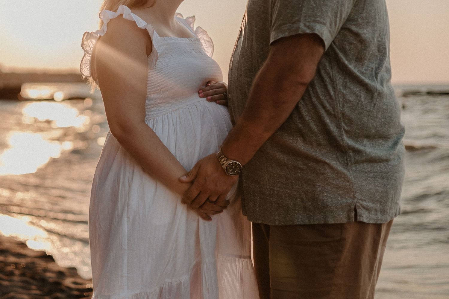 Close-up of couple holding hands on beach at sunset with waves crashing behind them.