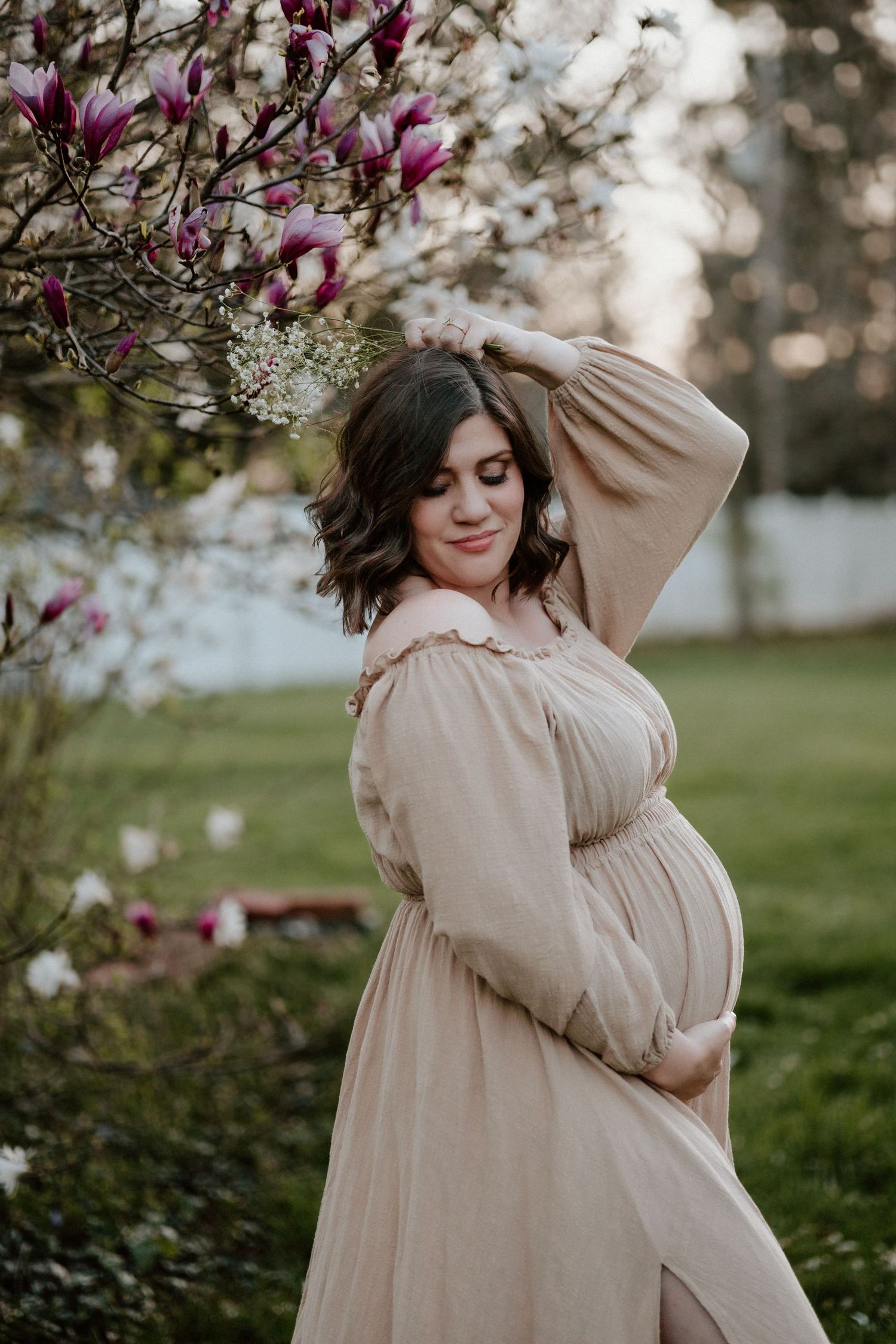 Maternity photo under blooming magnolia trees with a flowing beige dress.