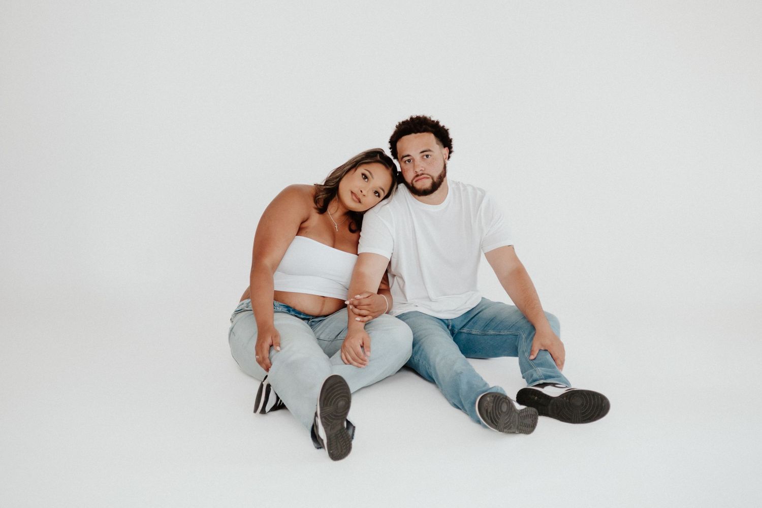 A casual couple sits together on the floor during a lifestyle photoshoot.