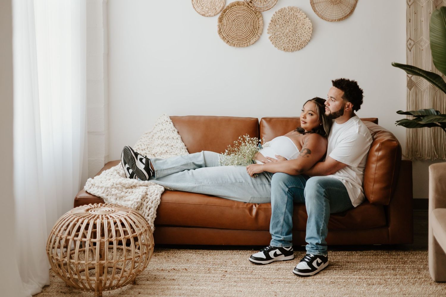 A couple relaxes together on a brown leather couch in their living room.
