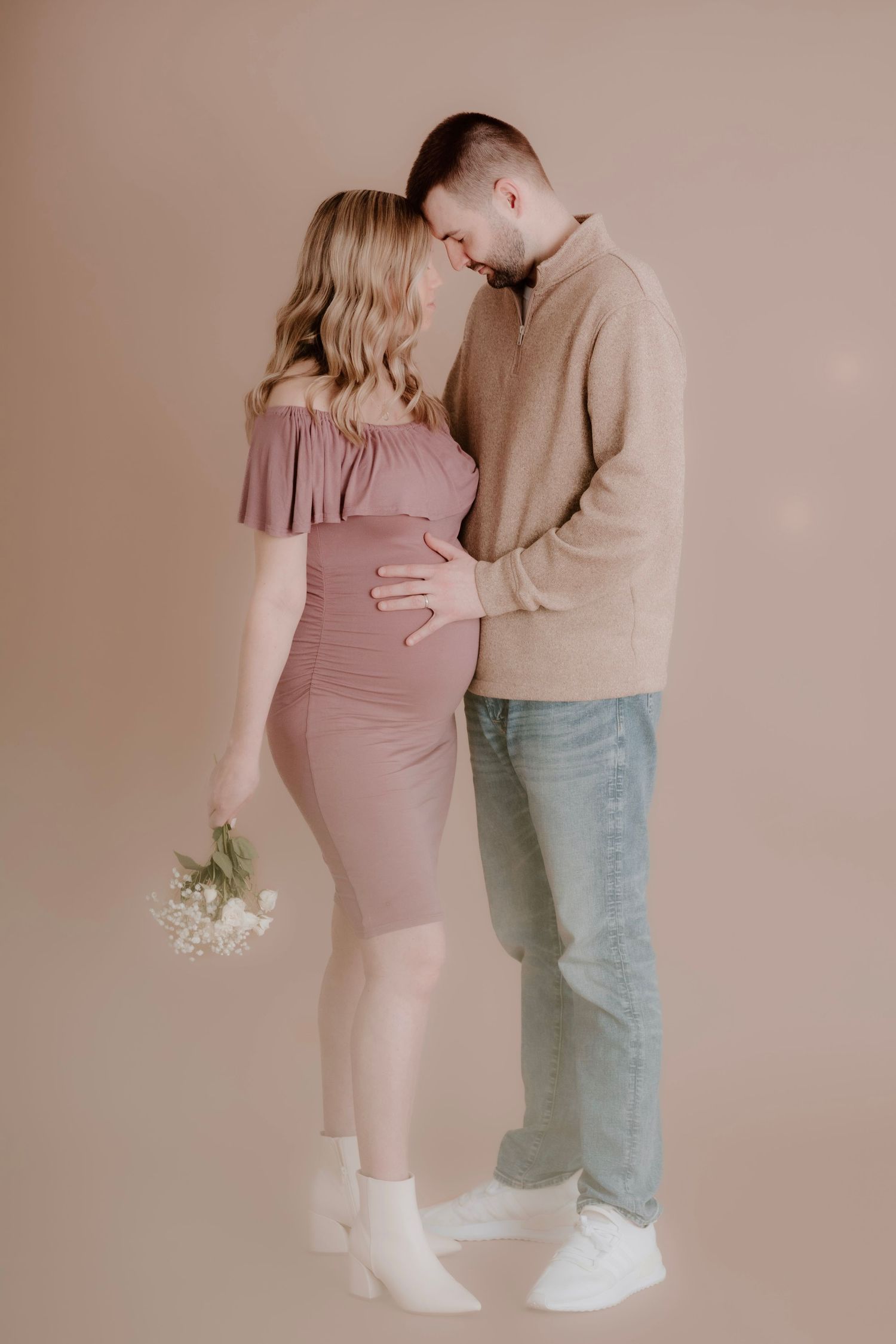 A tender maternity moment captured against a neutral background with soft lighting.