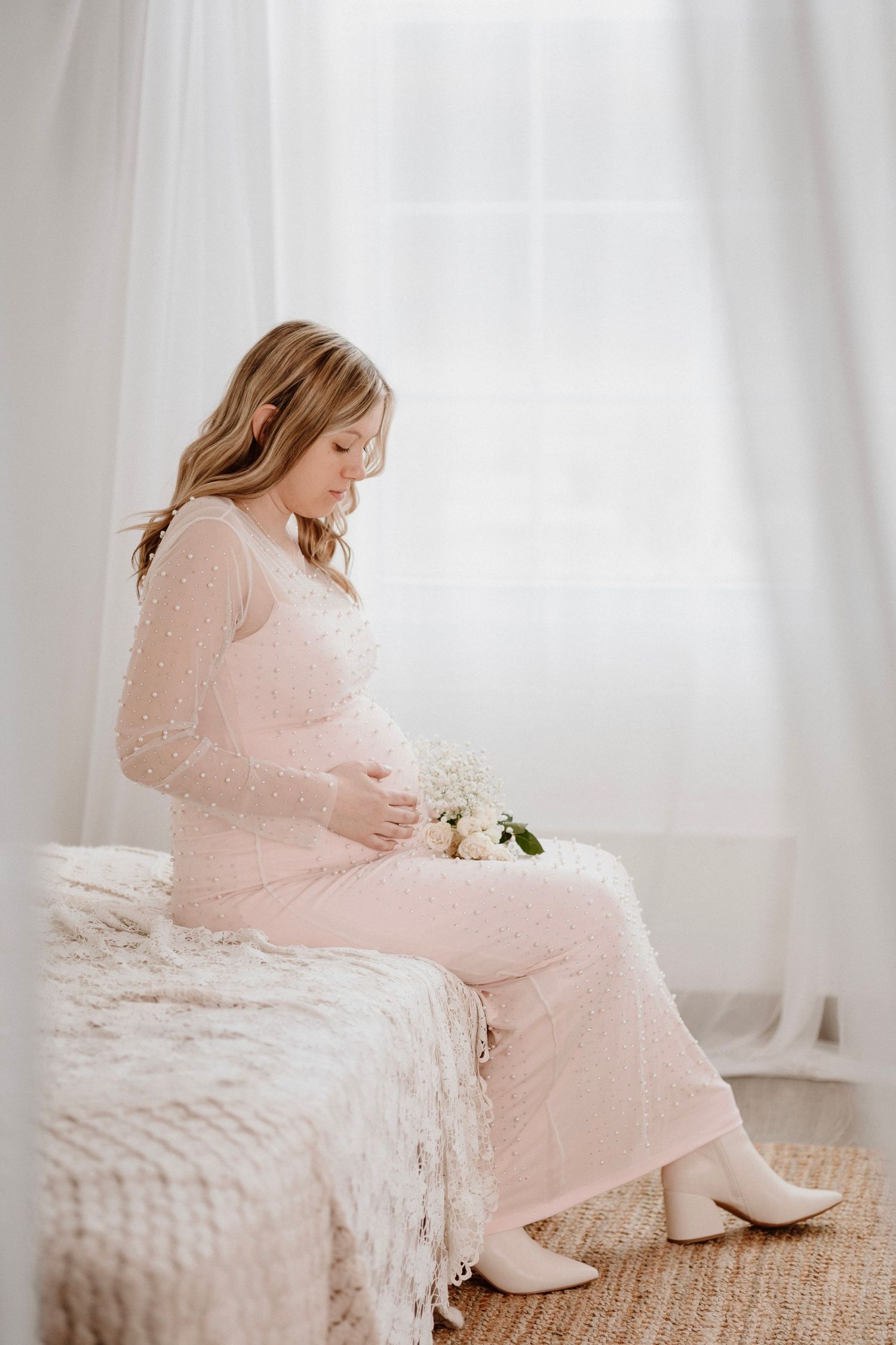 A maternal photoshoot featuring a pink pearl-embellished dress and white flowers.