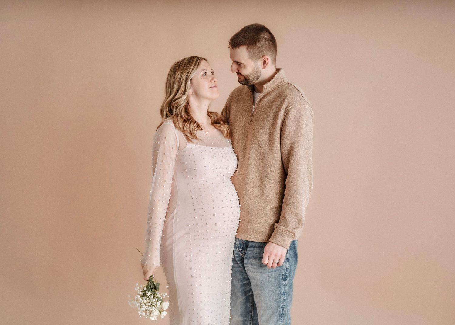 A maternity portrait featuring soft pink and beige tones with delicate flowers.
