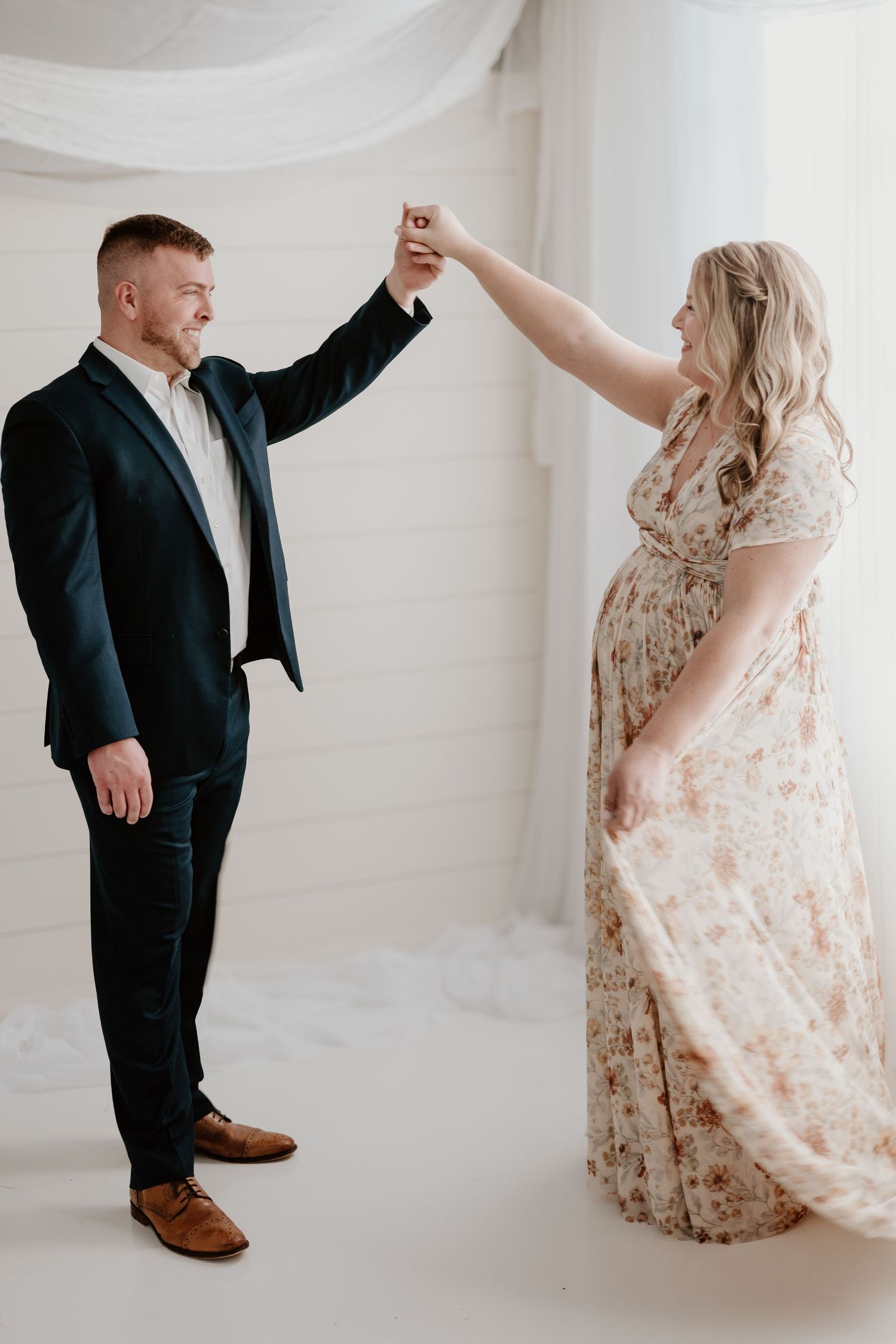 Playful maternity photo of couple dancing in white studio setting.