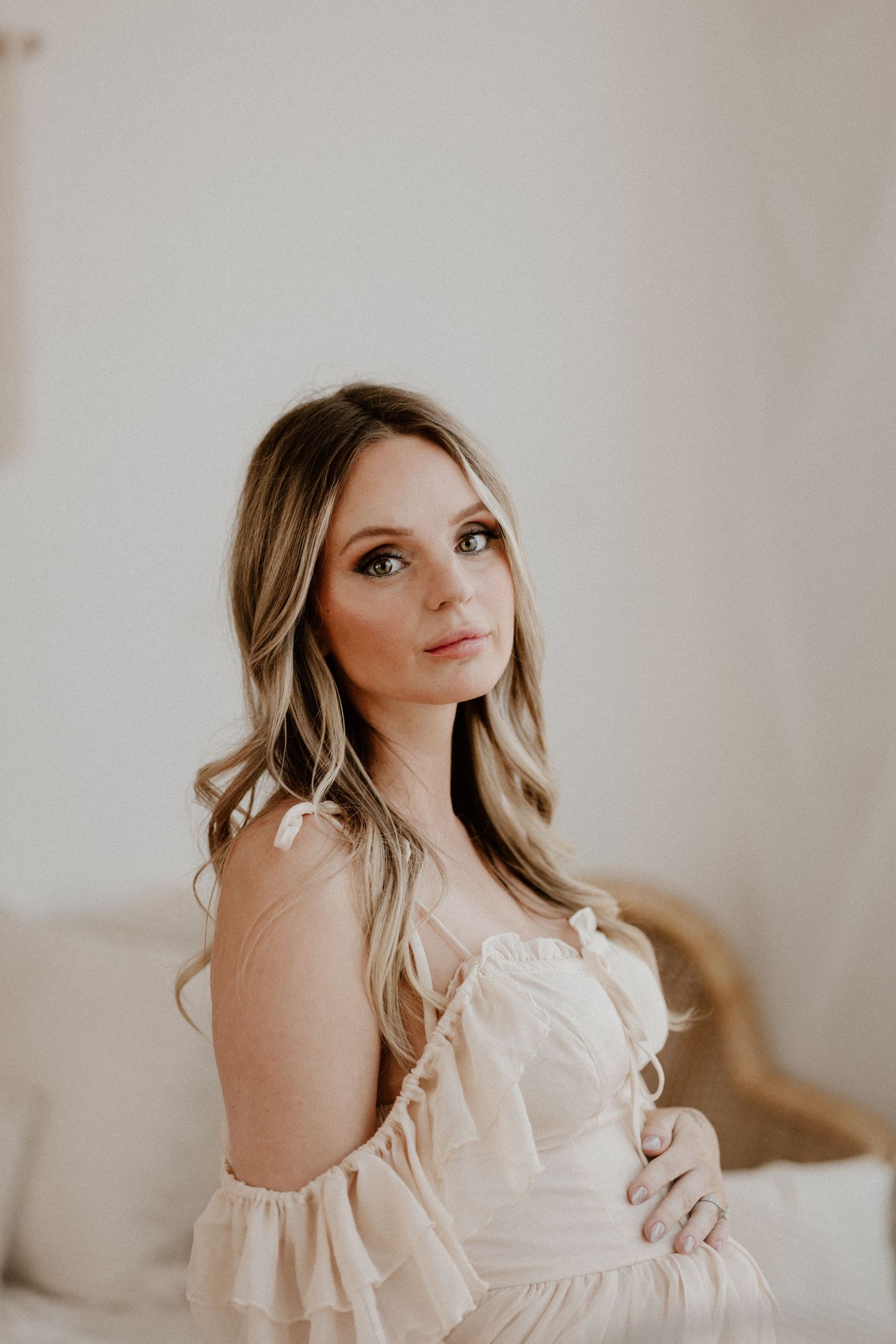 Side profile portrait of a woman in a flowing cream dress against a minimal background.