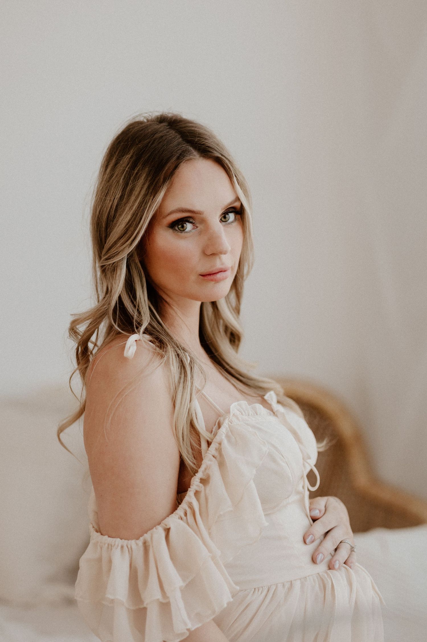 Soft portrait of a woman in a romantic off-shoulder cream dress in natural window light.