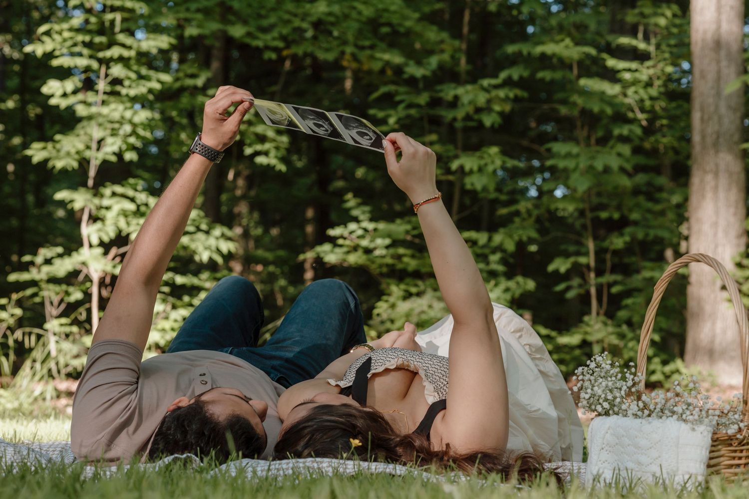 A couple lying on grass holding ultrasound photos above them in a playful pose.