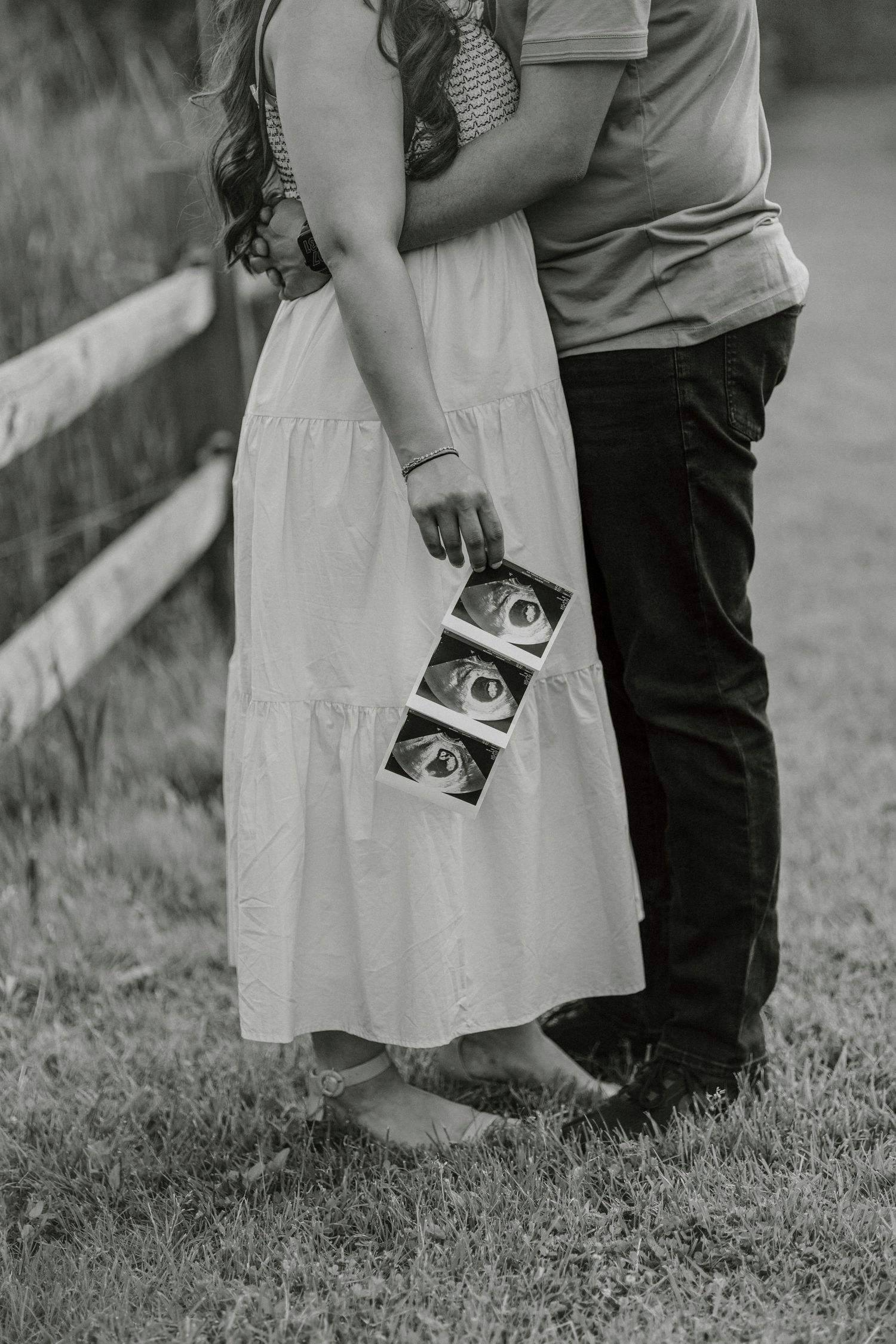A couple embracing while holding ultrasound photos, captured in black and white.